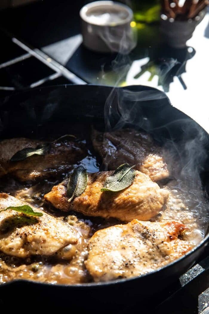 照片上的棕色鼠尾草黄油鸡Piccata在炉子上煎锅